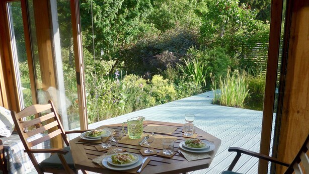 An outdoor dining area with a table set for two, surrounded by wooden chairs, overlooking a lush garden. - Victorian cottage, large gardens, near river, Hadrian's Wall & Allendale (Allendale)