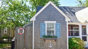 Una casa con techo a dos aguas, una ventana con contraventanas azules y una pequeña decoración de ancla debajo de la ventana.