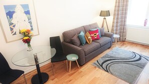 A modern living room with a grey sofa, a glass coffee table, a black chair, a small side table, and a grey rug. - Quiet one bedroom apartment in the heart of Edinburgh's West end (Edinburgh)