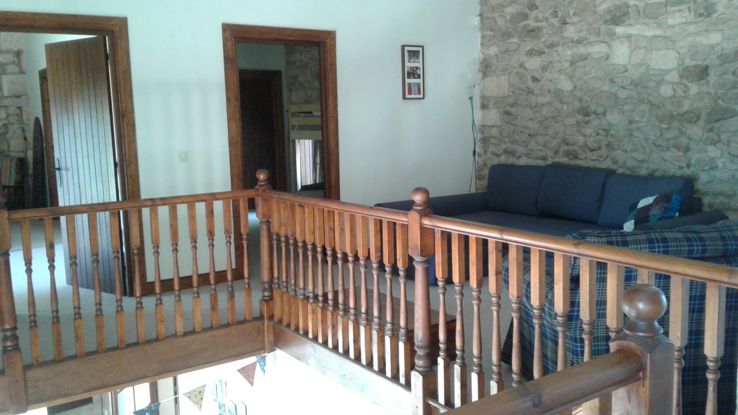 A staircase with wooden balusters leading to a living area with a stone wall and a blue sofa.