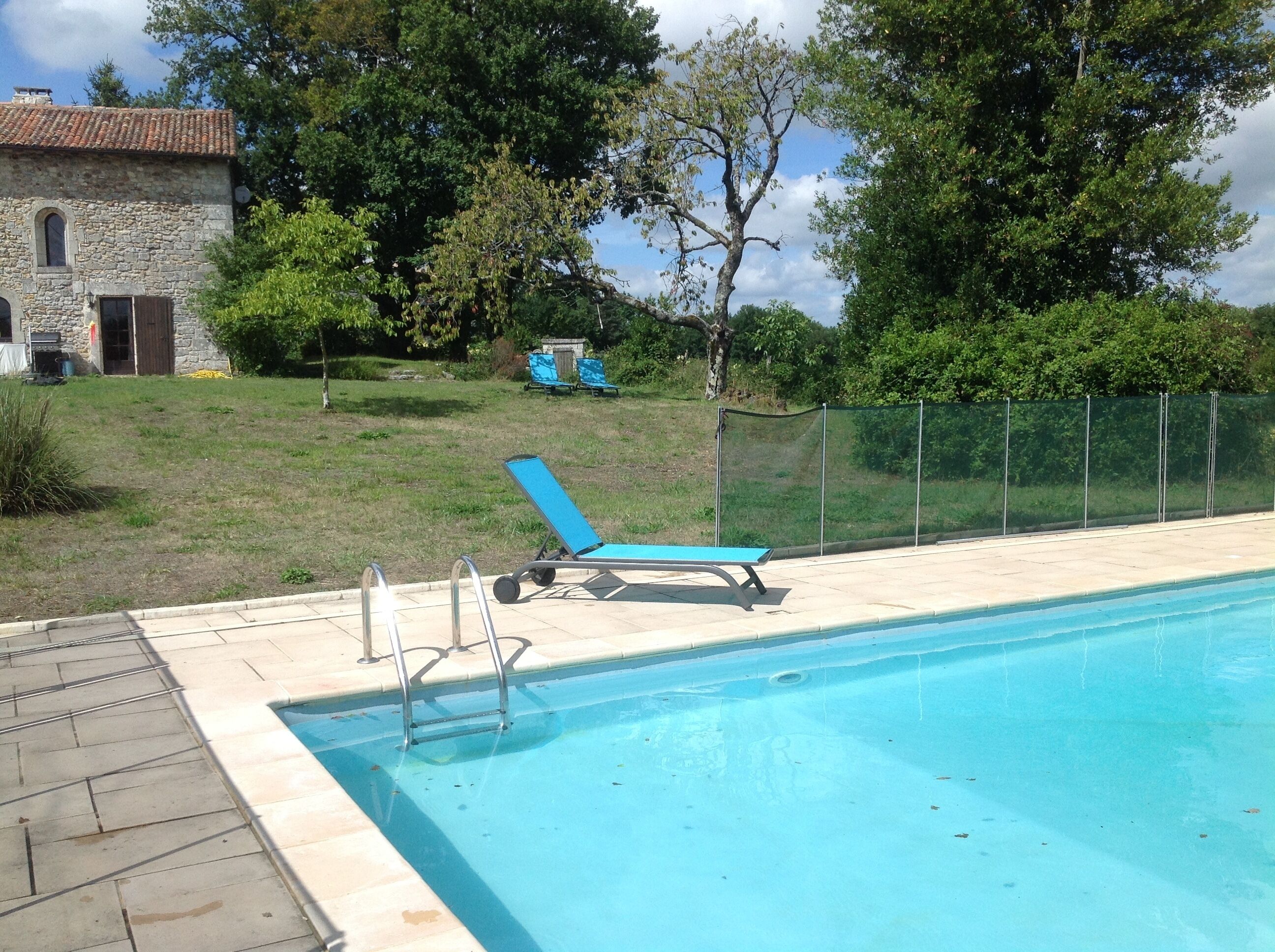 A swimming pool with a blue lounge chair and a stone building in the background.