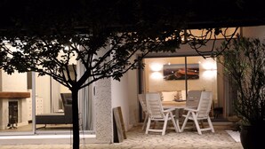 An outdoor patio with a table and chairs, a potted plant, and a view of the interior through glass doors.