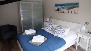 A bedroom with a bed, a nightstand, a lamp, a painting, and a wardrobe.