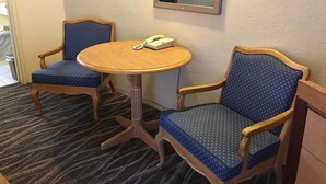 Une chambre d’hôtel avec une table ronde en bois, deux fauteuils bleus, un téléphone et un miroir au mur.
