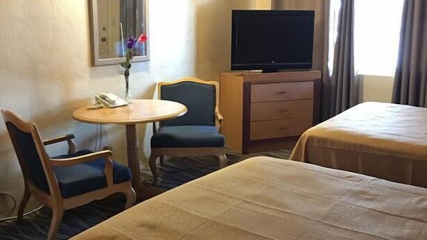 Une chambre d’hôtel avec deux lits, un téléviseur posé sur une commode en bois, une petite table ronde avec une chaise, et un miroir au mur.