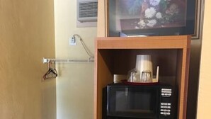 Une petite cuisine équipée comprenant un micro-ondes et une machine à café placés sur une étagère, un petit réfrigérateur en dessous et une bouche d’aération fixée au mur.