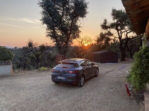 Um carro estacionado em uma entrada de automóveis de cascalho, com um edifício e árvores ao fundo.