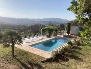 Piscina com espreguiçadeiras, uma palmeira e vista para montanhas ao longe.