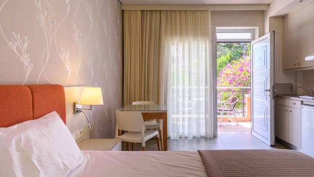Une chambre d’hôtel avec un lit, un bureau, une chaise, une lampe et une vue sur un balcon fleuri.