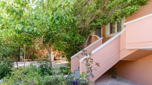Un escalier menant à un bâtiment à la façade de couleur pêche, entouré d’une végétation luxuriante et de diverses plantes.
