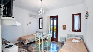 A small, tidy room with two beds, a table with chairs, a washing machine, and a television. - New Aurora By Checkin (Ierapetra)