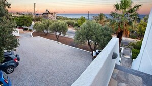 A residential area with a paved driveway, parked cars, and a view of the sea at sunset. - New Aurora By Checkin (Ierapetra)