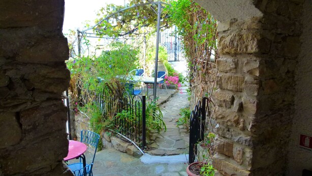 A stone archway leading to a courtyard with a metal pergola, potted plants, and outdoor seating. - Agriturismo Un Posto al Sole (Diano San Pietro)