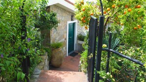 A stone building with a green door, surrounded by lush greenery and orange trees. - Agriturismo Un Posto al Sole (Diano San Pietro)