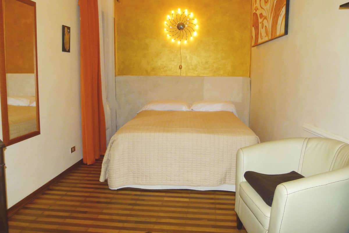 Hotellihuone, jossa on sänky, tuoli, peili ja seinään kiinnitetty valaisin.