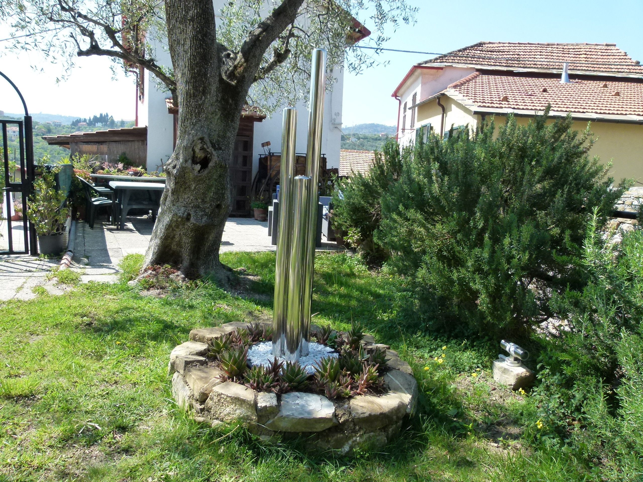A garden with a stone fountain, a tree, and a building in the background.