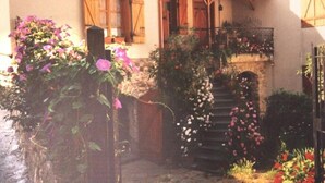 A rustic building with wooden shutters, a stone staircase, and a garden with various flowers. - Agriturismo Un Posto al Sole (Diano San Pietro)