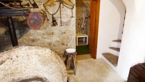 A rustic room with a large stone wheel, a wooden table with a chair, and a staircase leading to a door. - Agriturismo Un Posto al Sole (Diano San Pietro)