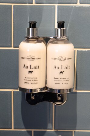 Two bottles of Au Lait hand lotion and creme handwash by Scottish Fine Soaps, mounted on a blue tiled wall. - Apple Pip (Fort Augustus)