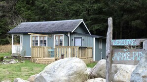 Un petit bâtiment en bois doté d’un porche, d’une pancarte d’accueil et de gros rochers au premier plan.
