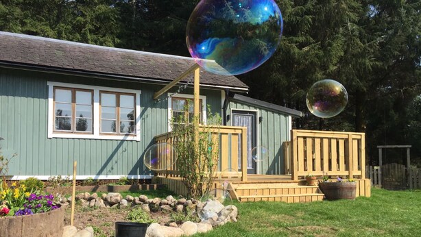 Une maison avec une terrasse en bois, un petit jardin fleuri et une clôture en bois.