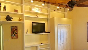 Ein Schlafzimmer mit einem Bett, einem Fernseher auf einem weißen Regal, einem Kleiderschrank und einem Deckenventilator.