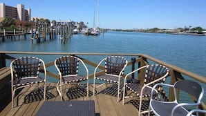 Eine Terrasse mit vier Korbstühlen und einem Tisch, mit Blick auf eine Marina mit Booten und Gebäuden im Hintergrund.