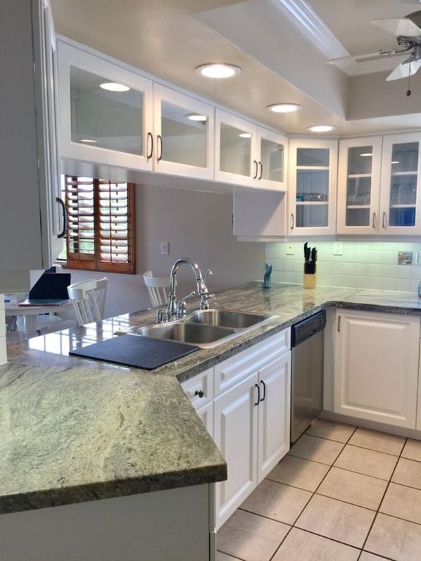 A modern kitchen with white cabinetry, granite countertops, and a built-in dishwasher.