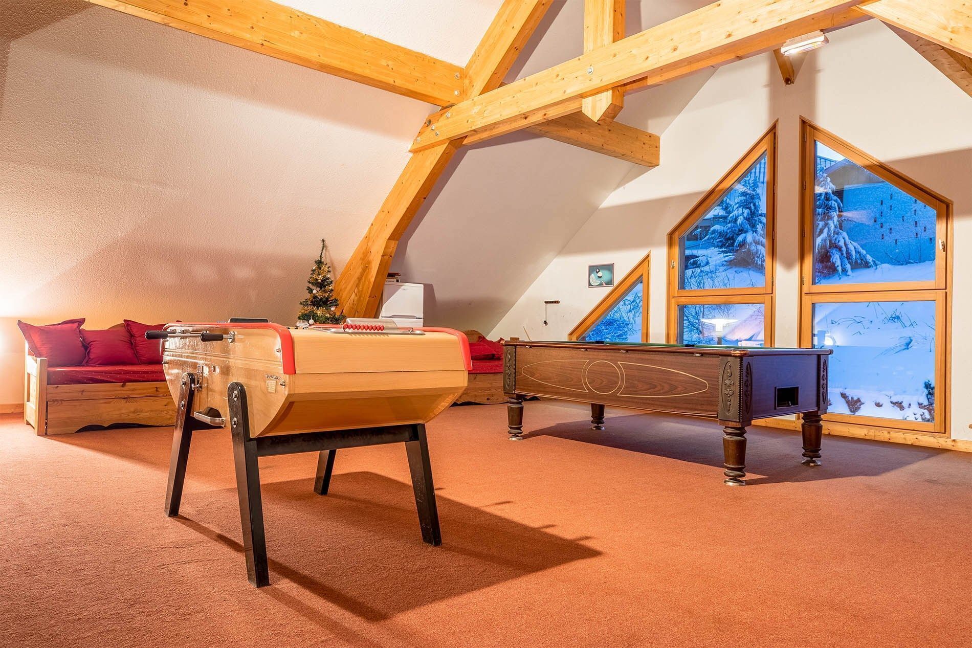 Een gezellige zolderkamer met een pooltafel, een rode bank en een kleine kerstboom.
