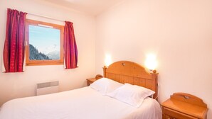 Ein ordentlich bezogenes Bett mit weißen Leinen, ein Holz-Kopfteil mit Herz-Aussparungen und ein Nachttisch mit einer Lampe.
