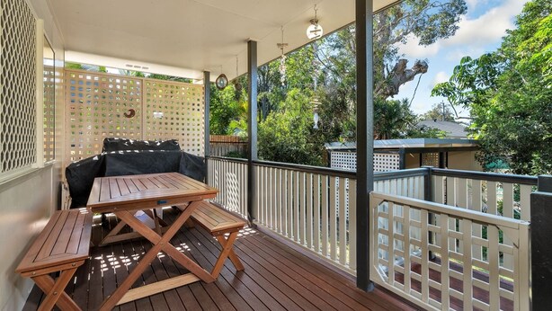 Un patio techado al aire libre con una mesa de madera y un sofá negro.
