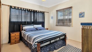 Un dormitorio con cama, mesitas de noche, ventilador de techo, ventana con persianas y puerta.