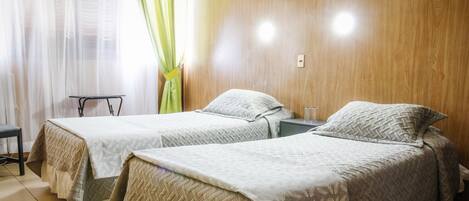 Habitación con dos camas, cada una con una colcha estampada, una mesita y una silla.