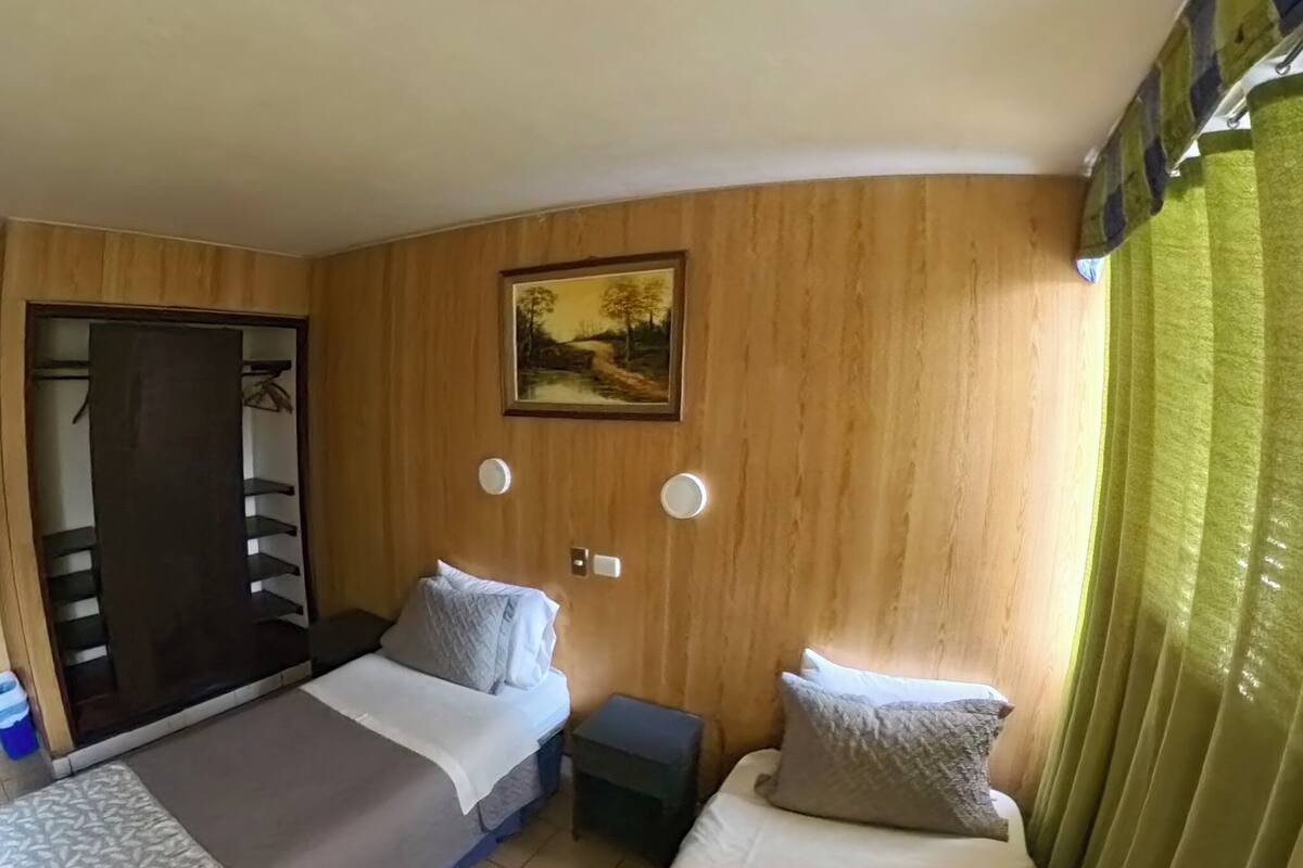 A hotel room with two beds, a wooden wardrobe, a painting on the wall, and a green curtain.