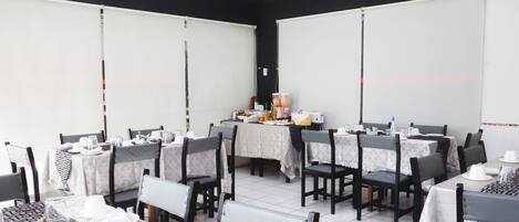 Un comedor con mesas dispuestas para el servicio, sillas y una estación de buffet.