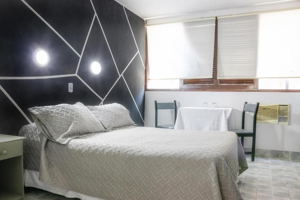 A bedroom with a bed, a nightstand, a window with blinds, and a table with chairs.
