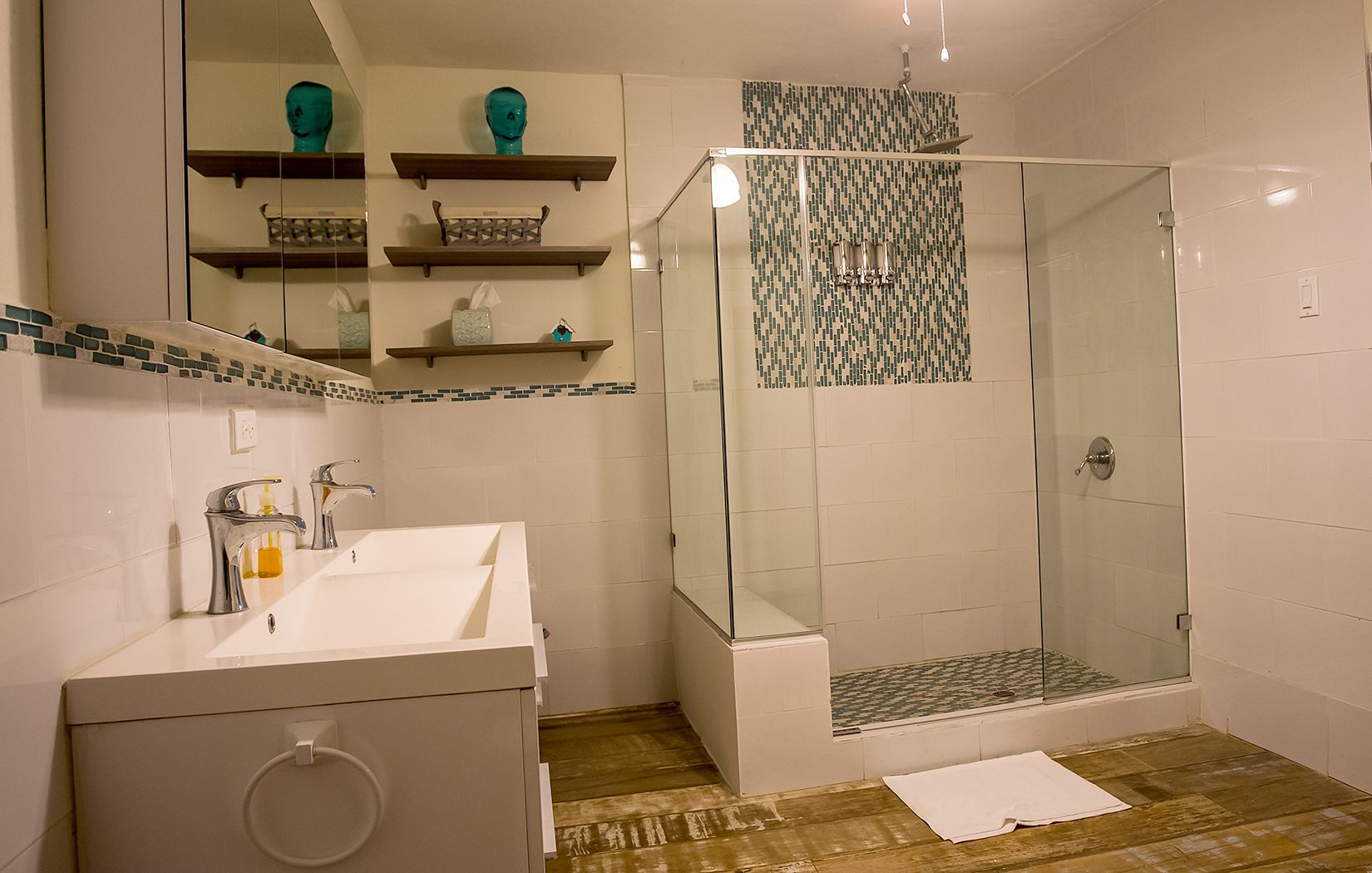 A modern bathroom with a glass-enclosed shower, a white sink with a mirror, and a wooden floor.