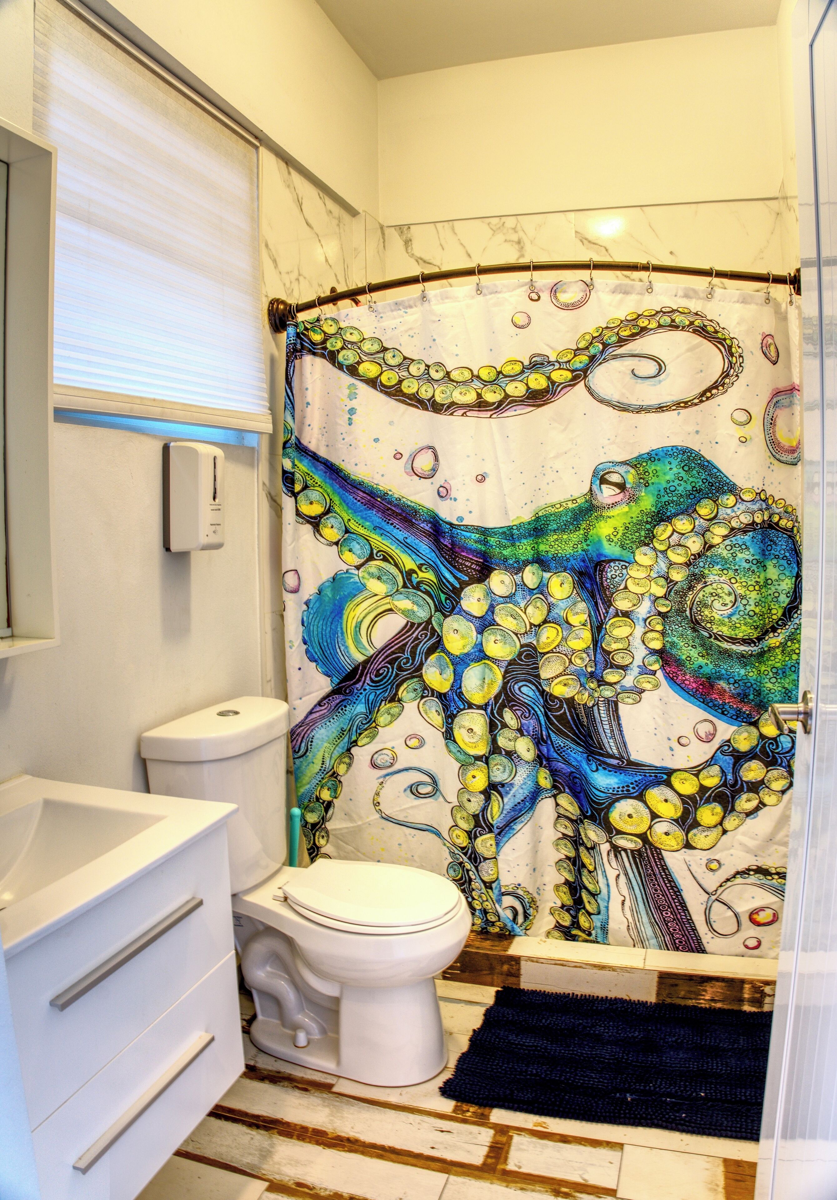 A bathroom with a white toilet, a white sink, and a shower curtain with a colorful octopus design.