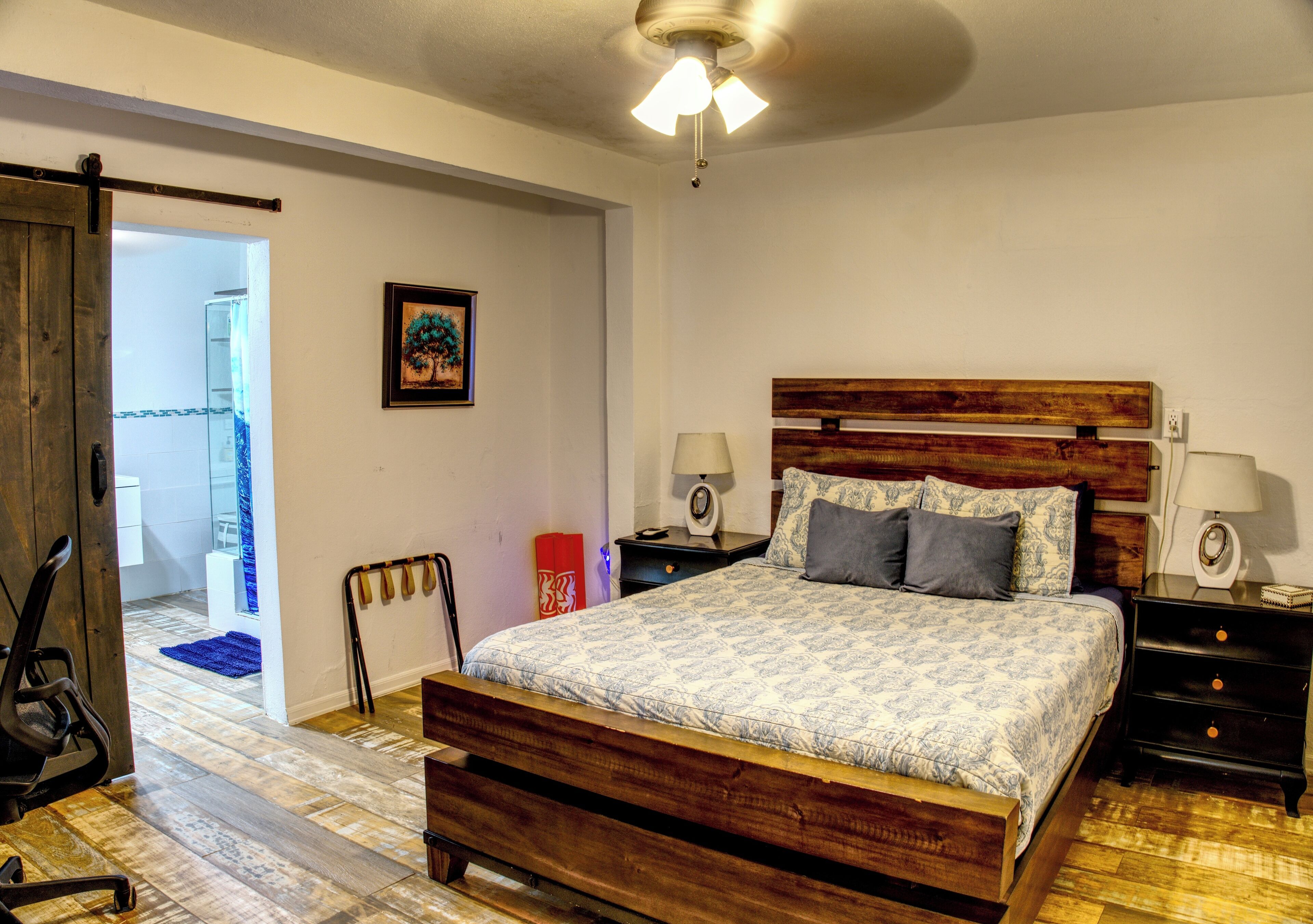 A bedroom with a wooden bed, two bedside tables, a ceiling fan, and a door leading to another room.