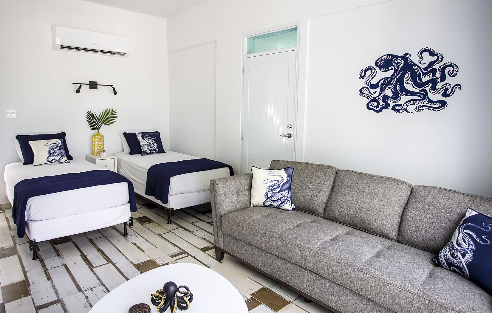 Een kamer met twee bedden, een grijze bank en een witte salontafel.