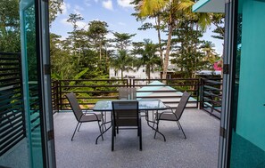 An outdoor patio area with a table and chairs, surrounded by a metal railing and palm trees. - The Beach Pad (Rincon)