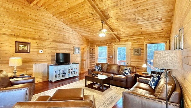 L’intérieur d’une cabane en rondins comprend un salon, des murs en bois, un ventilateur de plafond, un téléviseur et une cheminée.