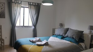 Ein ordentlich bezogenes Bett mit einer blauen und gelben Tagesdecke, zwei Kissen und zusammengerollten Handtüchern.