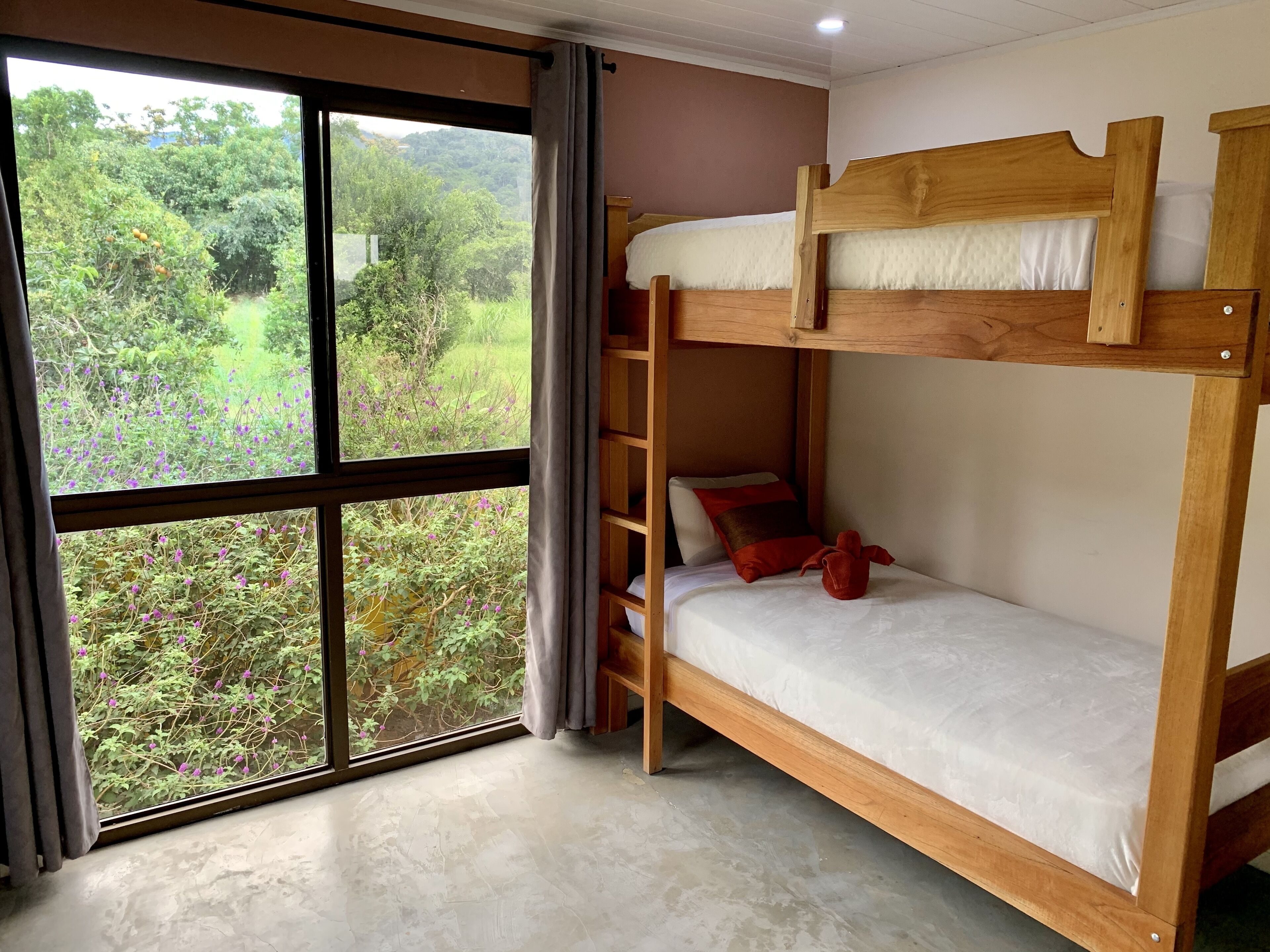 Une chambre avec des lits superposés et une grande fenêtre donnant sur un paysage verdoyant et des arbres.