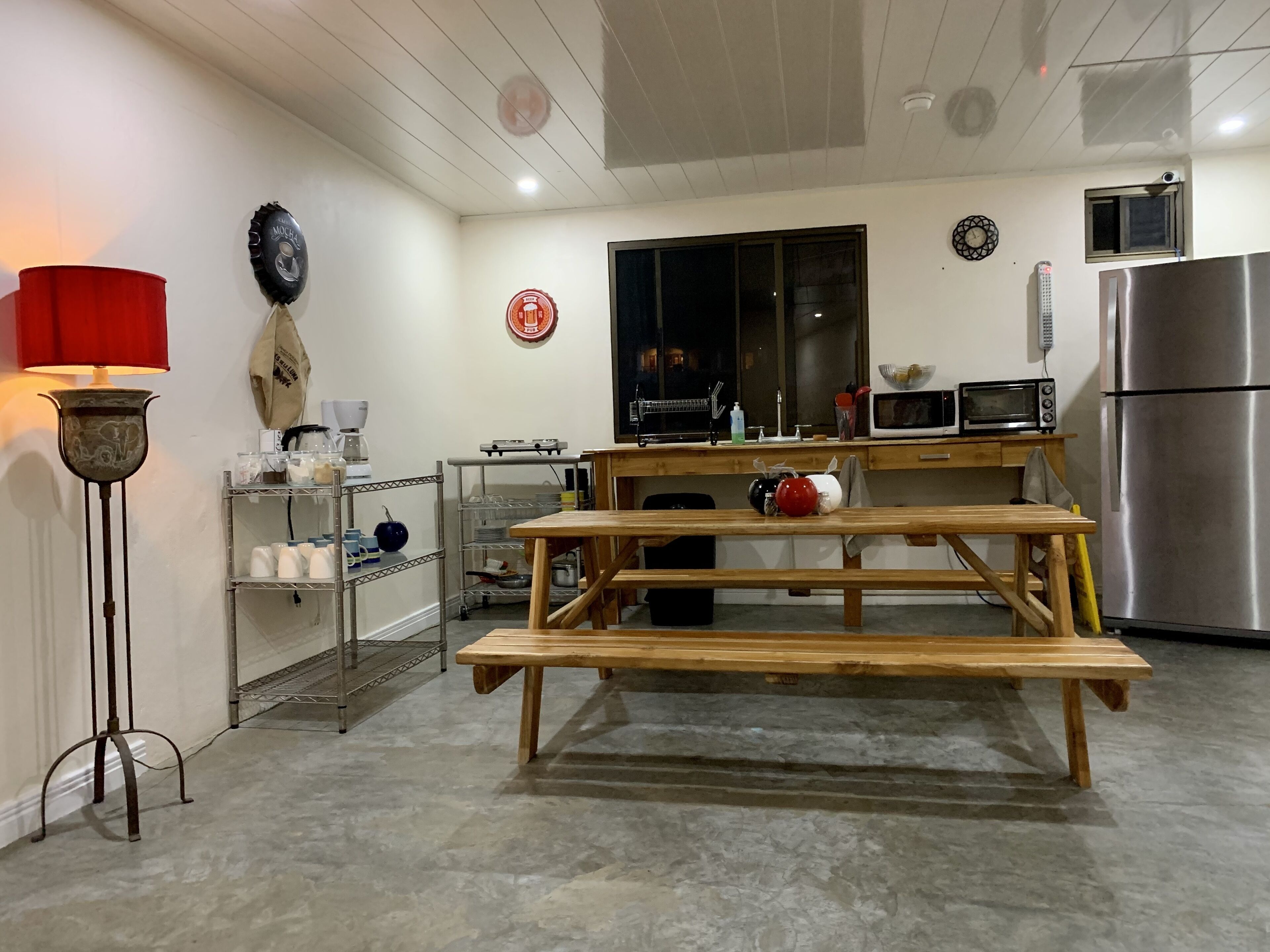 Una cocina con una mesa de madera, una lámpara roja, un refrigerador de acero inoxidable y un microondas.