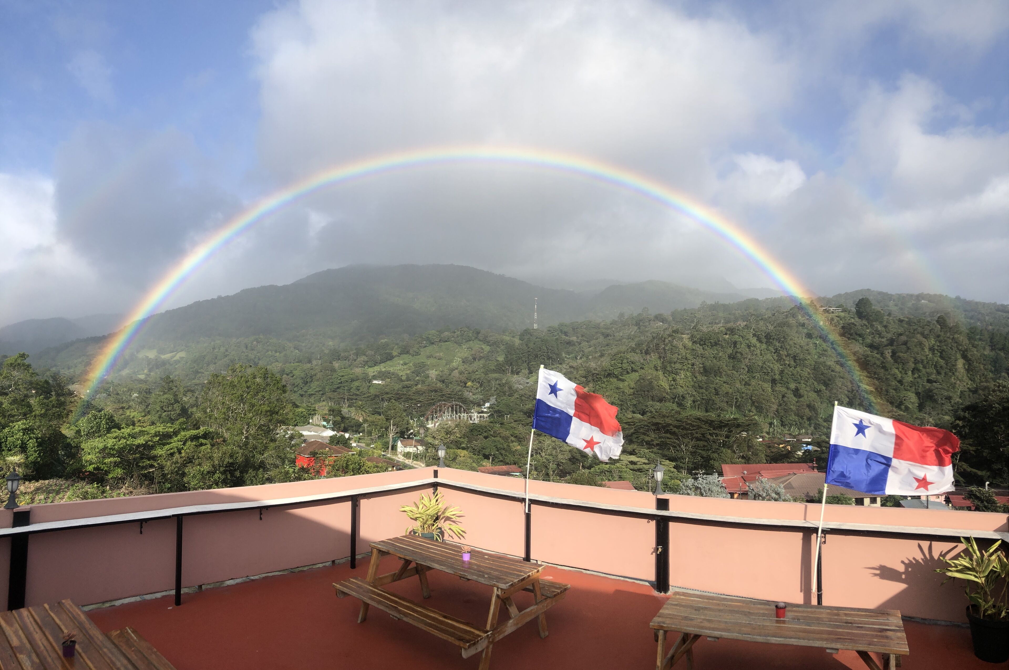 Une terrasse sur le toit, ornée de deux drapeaux, avec une table en bois et une vue sur une chaîne de montagnes.