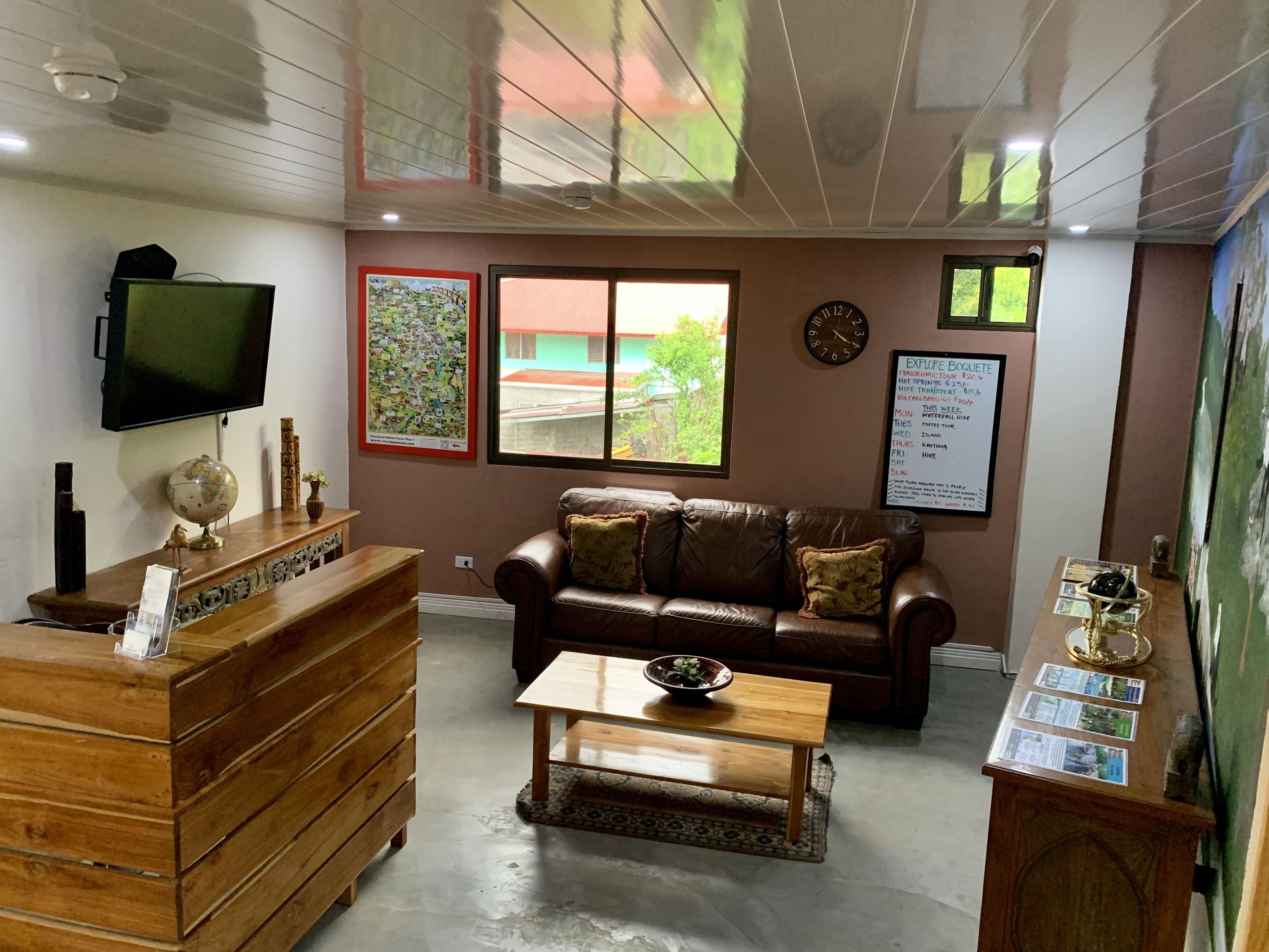 A reception area with a wooden desk, a leather sofa, a coffee table, a clock, and a window with a view of buildings.