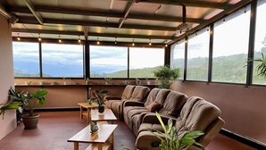 A spacious room with a large window, a sofa, a wooden table, and several potted plants. - Buena Vista Boquete (Boquete)