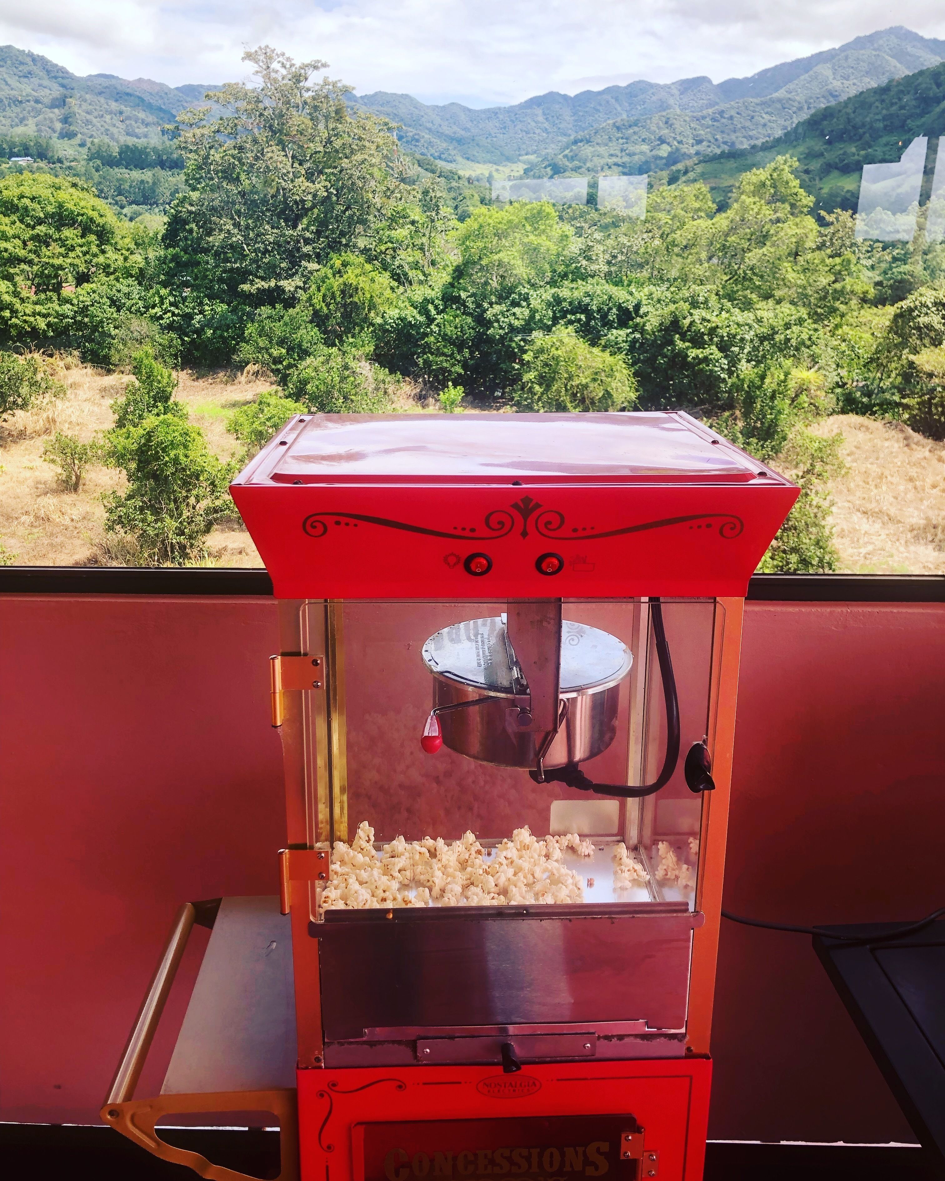 Eine rote Popcornmaschine mit Blick auf grüne Hügel und Berge im Hintergrund.