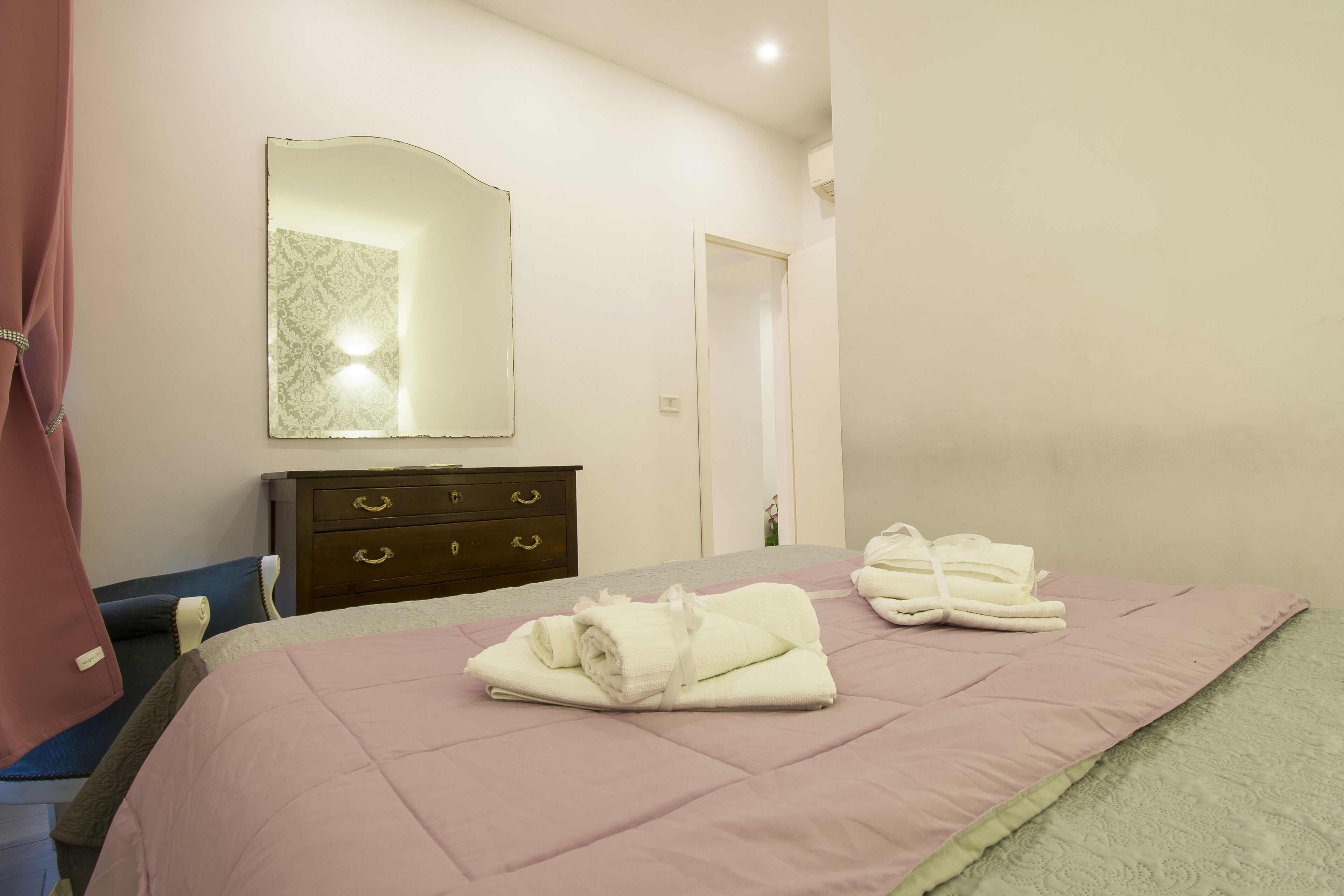 A neatly made bed with pink bedding, a wooden dresser with drawers, and a mirror on the wall.